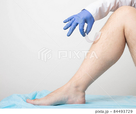 The doctor removes wax strips from the hair of the patient's legs on a white background. Leg hair removal concept. Copy space for text 84493729