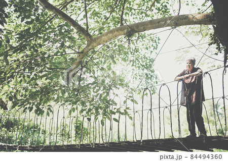 old elderly woman senior traveling on wooden hanging suspended rope bridge 84494360