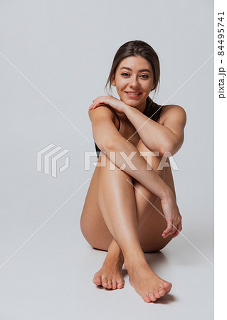 Young adorable woman in lingerie sitting on floor isolated over gray studio background. Natural beauty concept. Young adorable woman in lingerie sitting on floor isolated over gray studio background. Natural beauty concept. 84495741