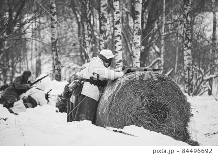 Re-enactor Dressed Like German Wehrmacht Infantry Soldier In World War II Aiming Rifle from Hay roll At Winter Day. Historical Re-enactment. Black And White Photo. WWII 84496692