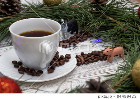 Christmas clock made of fir branches, clock hands of pine nuts, a cup of coffee and Christmas toys on a white wooden background, close-up, dog and piggy Christmas clock made of fir branches, clock hands of pine nuts, a cup of coffee and Christmas toys on a white wooden background, close-up, dog and piggy 84499425