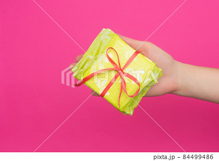 Female hand holding a stack of sanitary pads tied with a red ribbon in her hand, pink background, copy space, critical days 84499486