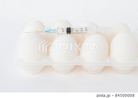 Chicken eggs on a white background on which lies a syringe in which there is a chemical substance, hormones, close-up Chicken eggs on a white background on which lies a syringe in which there is a chemical substance, hormones, close-up 84500008
