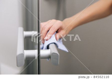 Cleaning glass door handles with an antiseptic wet wipe. Sanitize surfaces prevention in hospital and public spaces against corona virus. Woman hand using towel for cleaning home room door link. Cleaning glass door handles with an antiseptic wet wipe. Sanitize surfaces prevention in hospital and public spaces against corona virus. Woman hand using towel for cleaning home room door link. 84502110