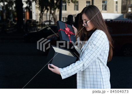 Stylish woman opened gift box. Happy young woman with gift on the street. Girl received a gift and opened it Stylish woman opened gift box. Happy young woman with gift on the street. Girl received a gift and opened it 84504073