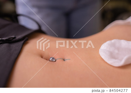 The first piercing. Dressing the earrings on the navel. Female piercing. The first piercing. Dressing the earrings on the navel. Female piercing. 84504277