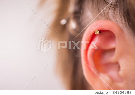 Professional placing the jewel of piercing on the ear with ball. Tragus type. 84504292