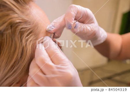 Professional placing the jewel of piercing on the temple on the head with ball. Tragus type. Professional placing the jewel of piercing on the temple on the head with ball. Tragus type. 84504319