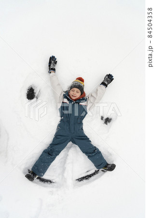 Snow angel made by kid in the snow. Boy lies in the snow. Winter vacation. Top view. Snow angel made by kid in the snow. Boy lies in the snow. Winter vacation. Top view. 84504358