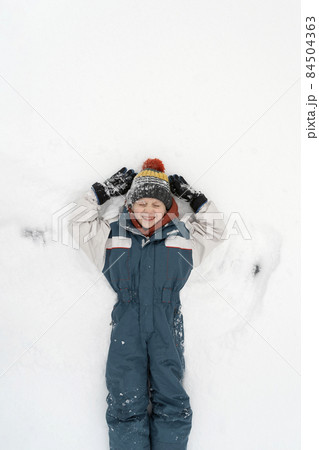 Cheerful boy lies in the snow and makes a snow angel. Happy childhood. Top view. Cheerful boy lies in the snow and makes a snow angel. Happy childhood. Top view. 84504363