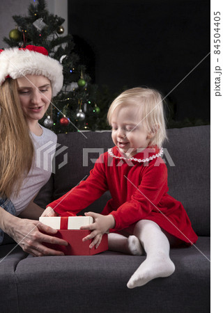Little girl and mom in Santa hat open Christmas gifts. 84504405