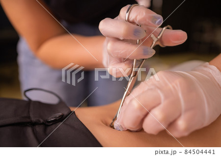 The first piercing. Dressing the earrings on the navel. Female piercing. 84504441