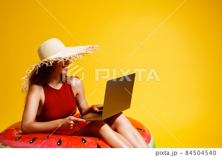 woman in straw hat sits in inflatable ring works on laptop on yellow background. freelance. Travel woman in straw hat sits in inflatable ring works on laptop on yellow background. freelance. Travel 84504540