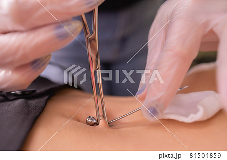 The first piercing. Dressing the earrings on the navel. Female piercing. The first piercing. Dressing the earrings on the navel. Female piercing. 84504859