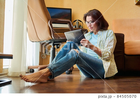 Middle aged woman looking at digital tablet, workplace with computer background 84505070