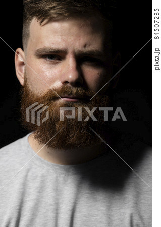 Close-up portrait of a handsome a brunette brutal bearded man in a grey t-shirt. Stylish and handsome man with a beard. 84507235