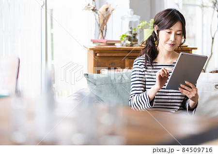自宅のリビングルームでタブレットPCを操作している女性 自宅のリビングルームでタブレットPCを操作している女性 84509716