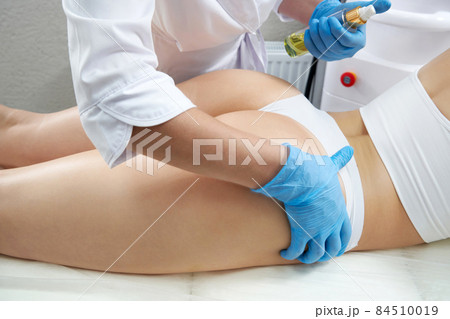 Cosmetologist moisturizing buttock skin of a woman with oil. Lifting, tightening concept Cosmetologist moisturizing buttock skin of a woman with oil. Lifting, tightening concept 84510019