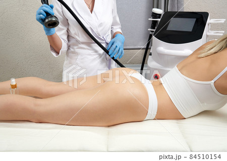 professional cosmetologist using ultrasound cavitation machine on a female buttock 84510154