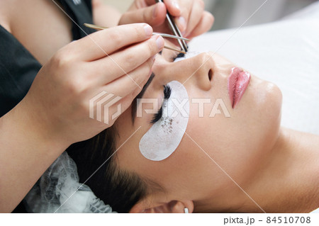 Eyelash extension procedure with tweezers in beauty salon 84510708