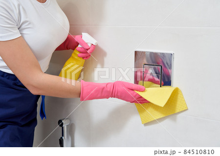 Hands wearing rubber protective gloves cleaning toilet flush button. Disinfection concept Hands wearing rubber protective gloves cleaning toilet flush button. Disinfection concept 84510810