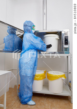 Technologist wearing PPE protective suit, mask, gloves working with big plastic bucket in research laboratory Technologist wearing PPE protective suit, mask, gloves working with big plastic bucket in research laboratory 84510869