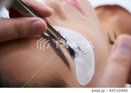 Eyelash extension procedure with tweezers in beauty salon 84510966