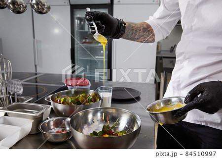 Closeup of chef hands preparing salad pouring sauce in a restaurant kitchen 84510997