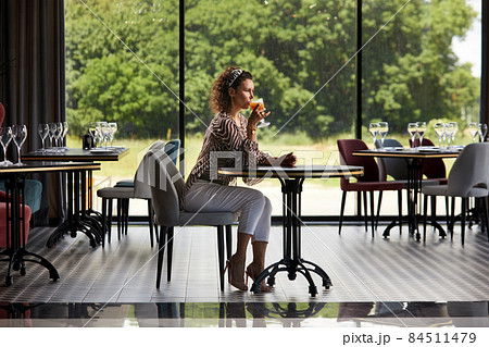 Beautiful young curly woman sitting in a cafe drinking fresh orange juice and waiting for her friend Beautiful young curly woman sitting in a cafe drinking fresh orange juice and waiting for her friend 84511479