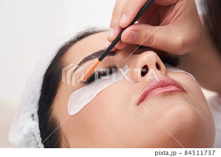 Cosmetologist making eyelash extention and correction using brush 84511737