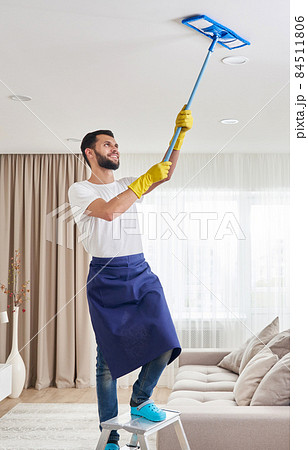 Man cleaning ceiling and lamps in living room. House cleaning service concept. 84511806