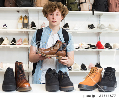 Positive teenager choosing fashionable winter boots in shoe store Positive teenager choosing fashionable winter boots in shoe store 84511877