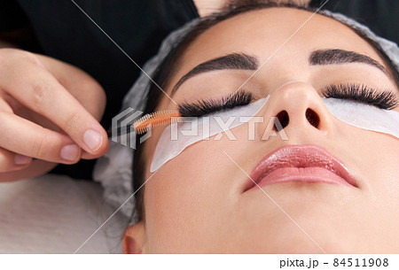 Cosmetologist making eyelash extention and correction using brush 84511908