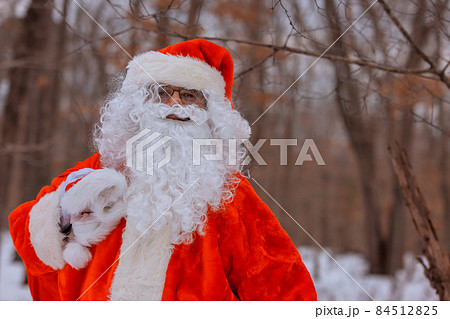 On cold winter day in a red Santa hat walk in a beautiful snowy forest, carry Christmas present gifts stand with their backs 84512825