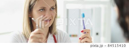 Woman doctor dentist shows patient toothbrush and dental instrument Woman doctor dentist shows patient toothbrush and dental instrument 84515410