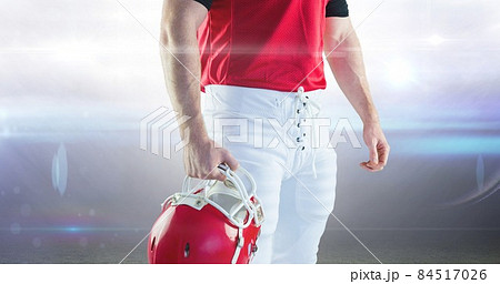 Midsection of muscular male american football player holding helmet against illuminated stadium 84517026