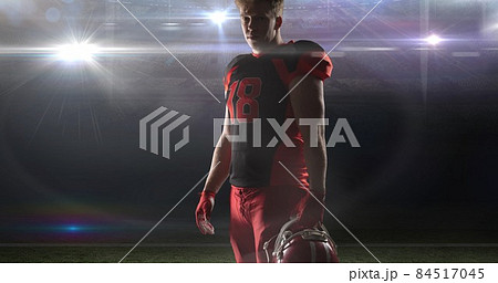 Portrait of confident player wearing jersey holding helmet at illuminated american football stadium 84517045