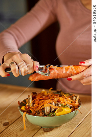 Women scraps peels carrots vegetable peeling, throws in compost bucket, organic composting 84519850