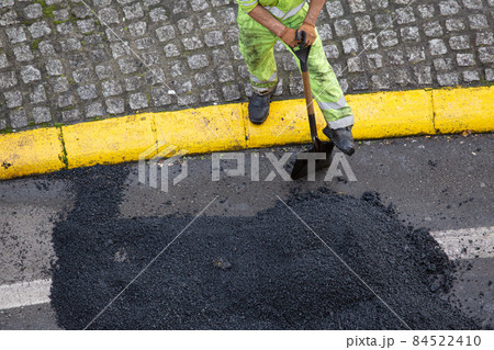 Worker with a shovel taking a break during the repair of a road with asphalt on city street. High angle view 84522410