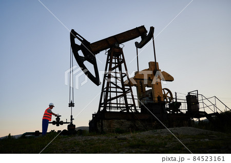 Capable professional inspector checking serviceability of pump jack during shift job at crude oil station, Caucasian man developing drilling rig and extract natural resources at refinery digger Capable professional inspector checking serviceability of pump jack during shift job at crude oil station, Caucasian man developing drilling rig and extract natural resources at refinery digger 84523161