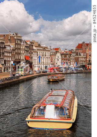 Amsterdam city with tourist boats on canal during springtime in Netherlands. Amsterdam city with tourist boats on canal during springtime in Netherlands. 84524655