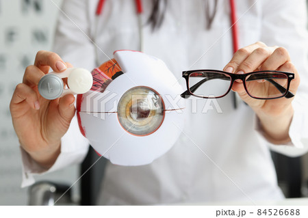 Ophthalmologist doctor holding eyeglasses and lenses near artificial model of eye closeup Ophthalmologist doctor holding eyeglasses and lenses near artificial model of eye closeup 84526688