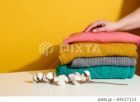 woman holding a stack of knitted folded sweaters on a yellow background. Washing clothes, cleaning things woman holding a stack of knitted folded sweaters on a yellow background. Washing clothes, cleaning things 84527113