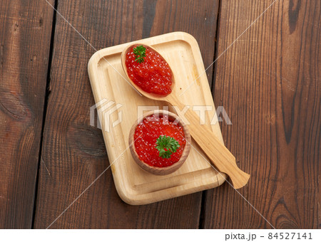 red caviar of pink salmon lies in a wooden spoon on a cutting board. Brown wooden table red caviar of pink salmon lies in a wooden spoon on a cutting board. Brown wooden table 84527141