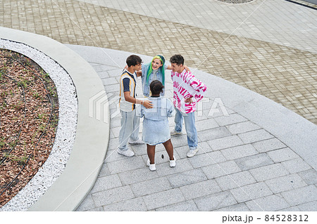 Diverse stylish students embracing and laughing while walking at the street 84528312