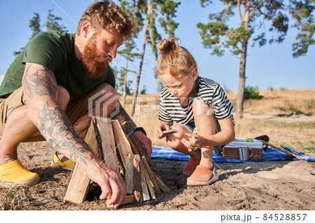 Father and daughter making fire from logs on coast Father and daughter making fire from logs on coast 84528857