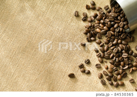 麻の上にマグカップから溢れ出るコーヒー豆 麻の上にマグカップから溢れ出るコーヒー豆 84530365