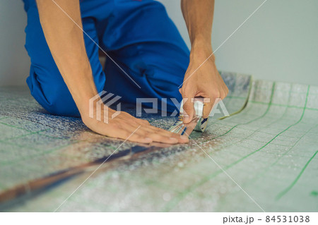 Master installs the overlapping thermal insulation in the room. Floor heating installation. Male hand holds reinforced tape. Repair in the apartment, floor insulation 84531038