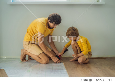 Father and son installing new wooden laminate flooring on a warm film floor. Infrared floor heating system under laminate floor 84531141