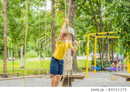 Little boy in a rope park. Active physical recreation of the child in the fresh air in the park. Training for children Little boy in a rope park. Active physical recreation of the child in the fresh air in the park. Training for children 84531173